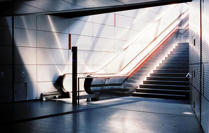 Sunlight illuminates an escalator and a staircase in a modern building.