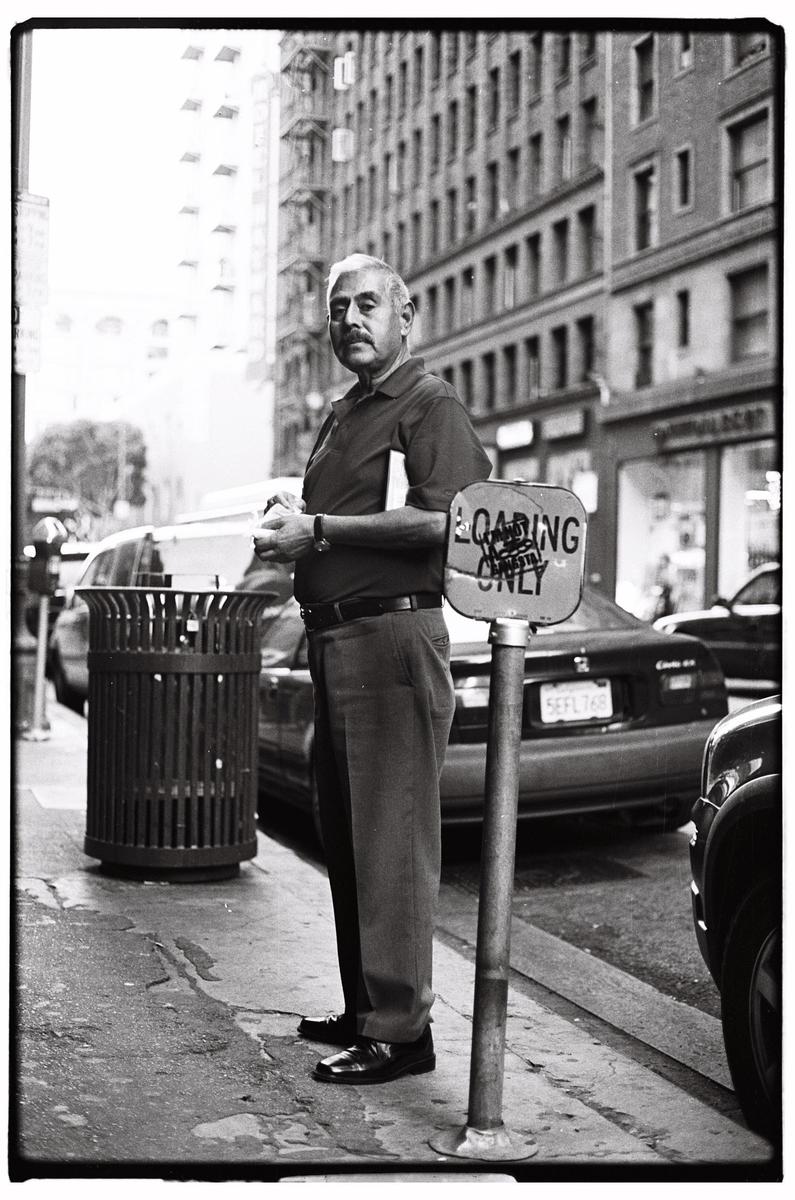 A man stands on a city sidewalk next to a trash can and a "loading only" sign.