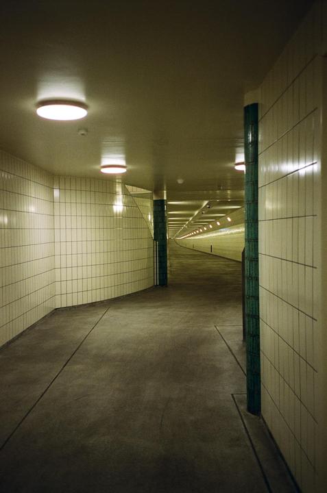 A long, empty tunnel with tiled walls and illuminated ceilings stretches into the distance.