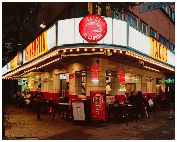 A brightly lit taco restaurant with outdoor seating is shown at night.