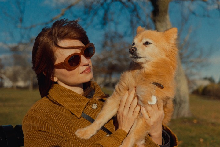 A woman wearing sunglasses holds a small dog in a park.
