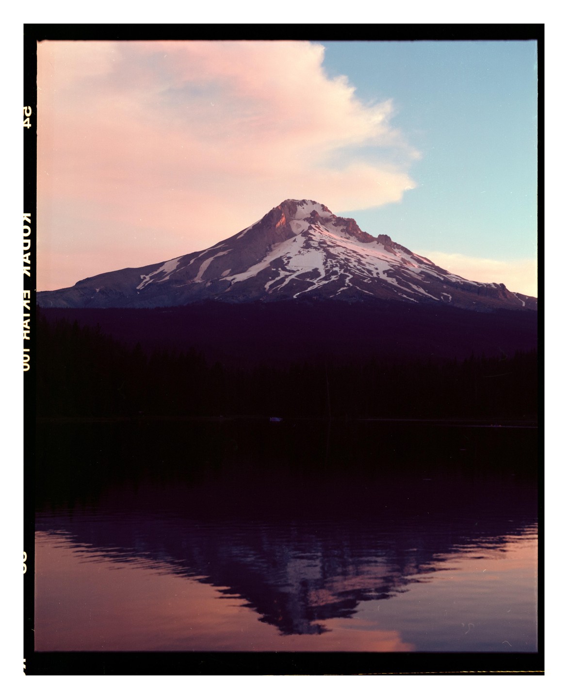 A snow-capped mountain is reflected in a body of water under a sky with pink clouds.