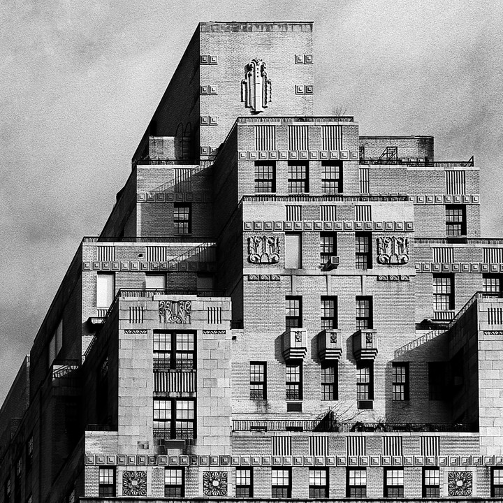 A tall, stepped building with many windows and decorative brickwork is shown from an upward-looking perspective.