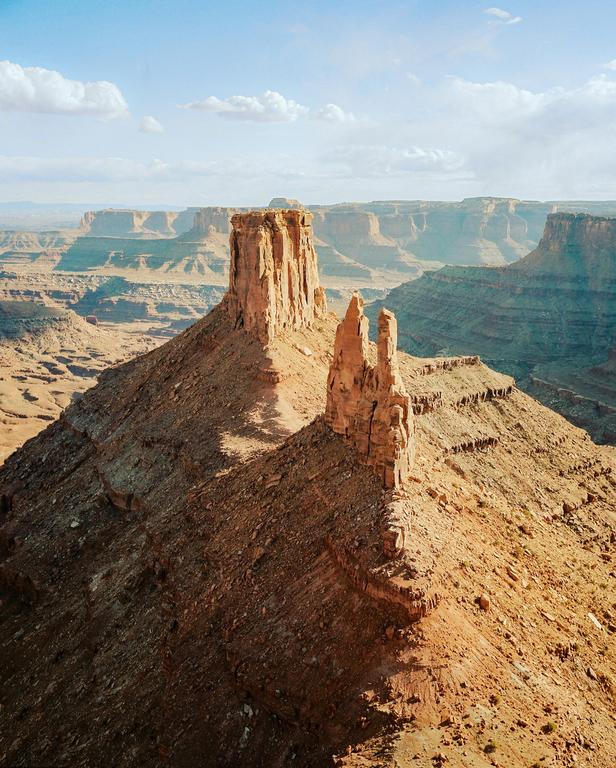 Two large rock formations stand prominently in a vast canyon landscape under a partly cloudy sky.