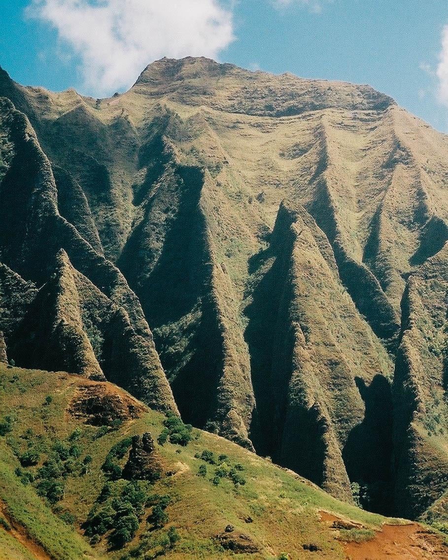 A mountain range with sharp ridges and valleys is visible under a blue sky with a few clouds.