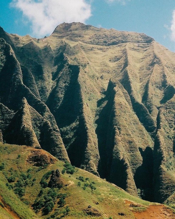 A mountain range with sharp ridges and valleys is visible under a blue sky with a few clouds.