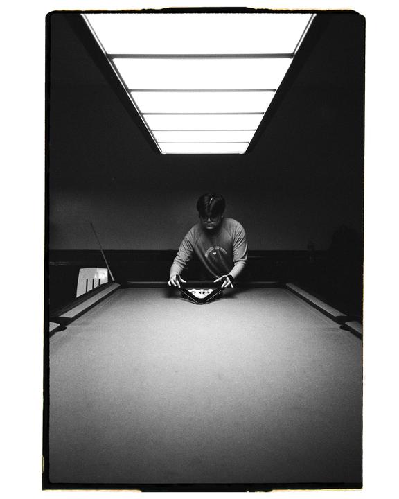 A man racks billiard balls on a pool table under a bright overhead light.
