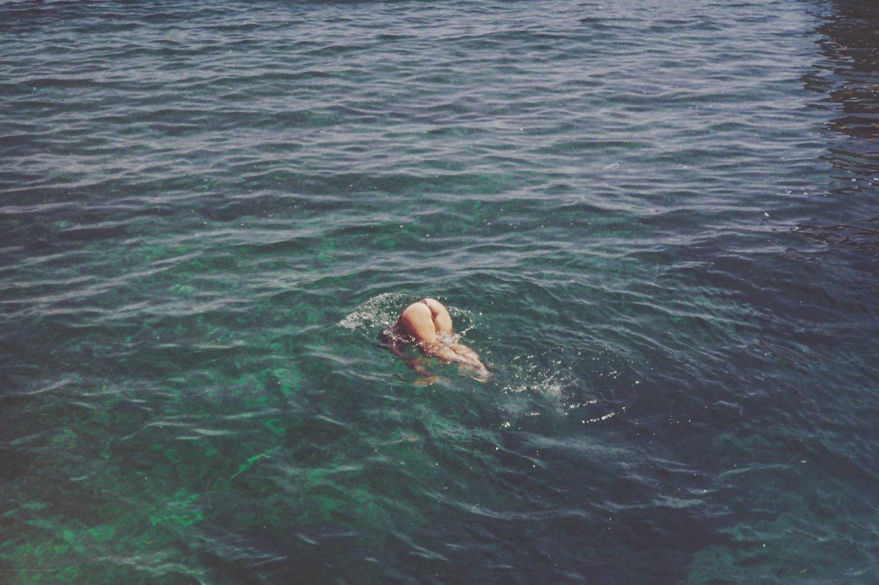 A person dives into clear blue water, with their lower body visible above the surface.