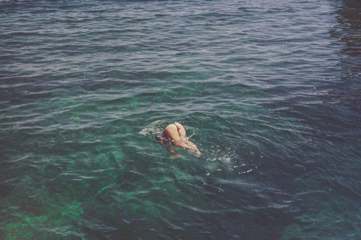 A person dives into clear blue water, with their lower body visible above the surface.