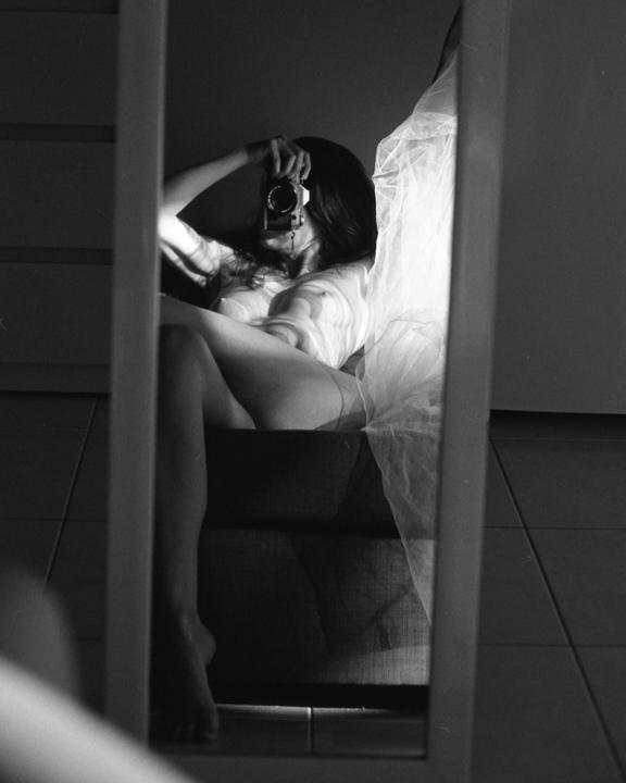 A woman takes a self-portrait in a mirror, holding a camera to her face.