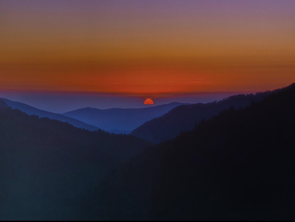 The sun sets over a mountain range with a colorful sky.