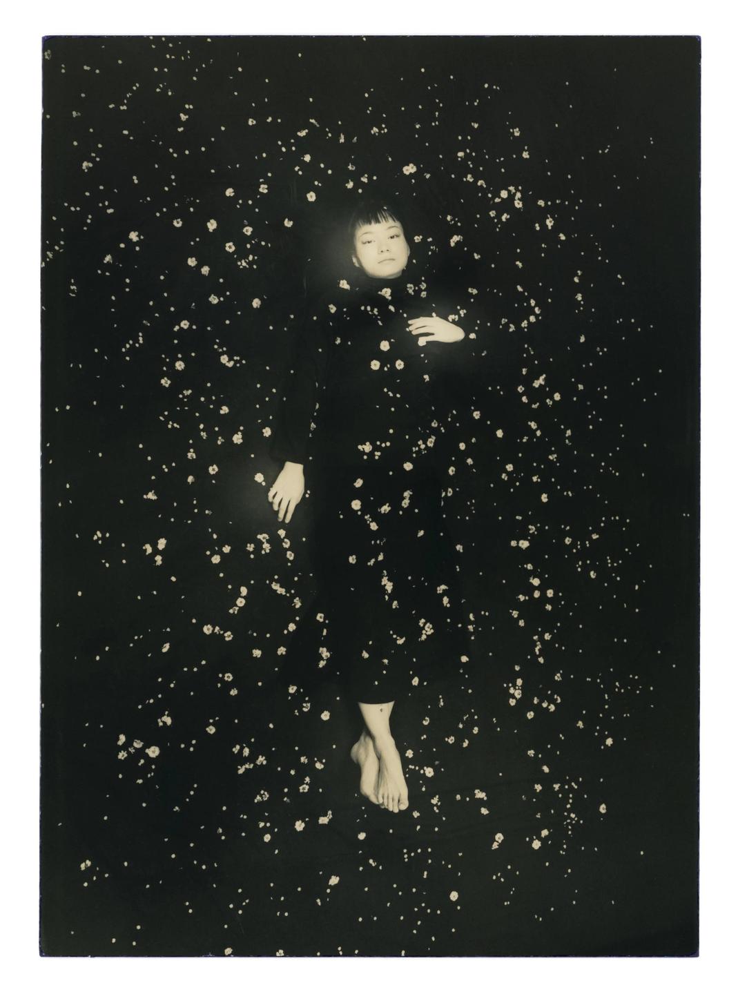 A woman lies on a dark surface covered with small, light-colored specks.