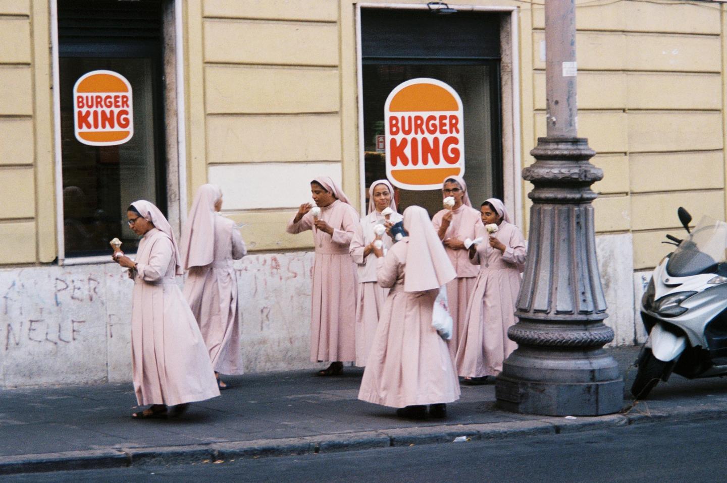 A group of nuns in pink habits eat ice cream cones on a street in front of a Burger King.