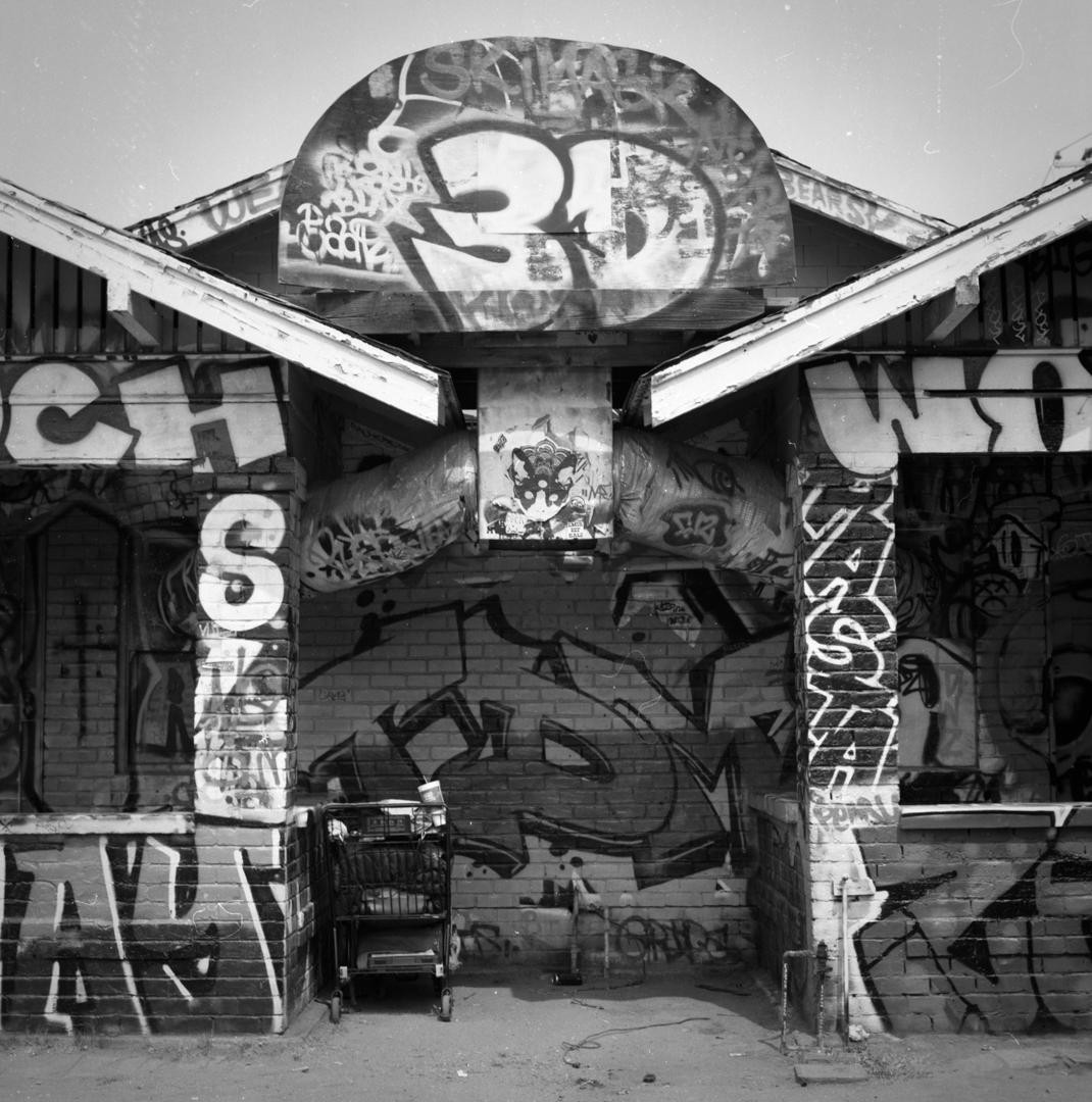 A shopping cart sits in front of a graffiti-covered brick building with a curved sign.