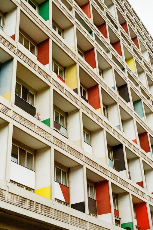 A man stands on a balcony of a building with colorful panels.