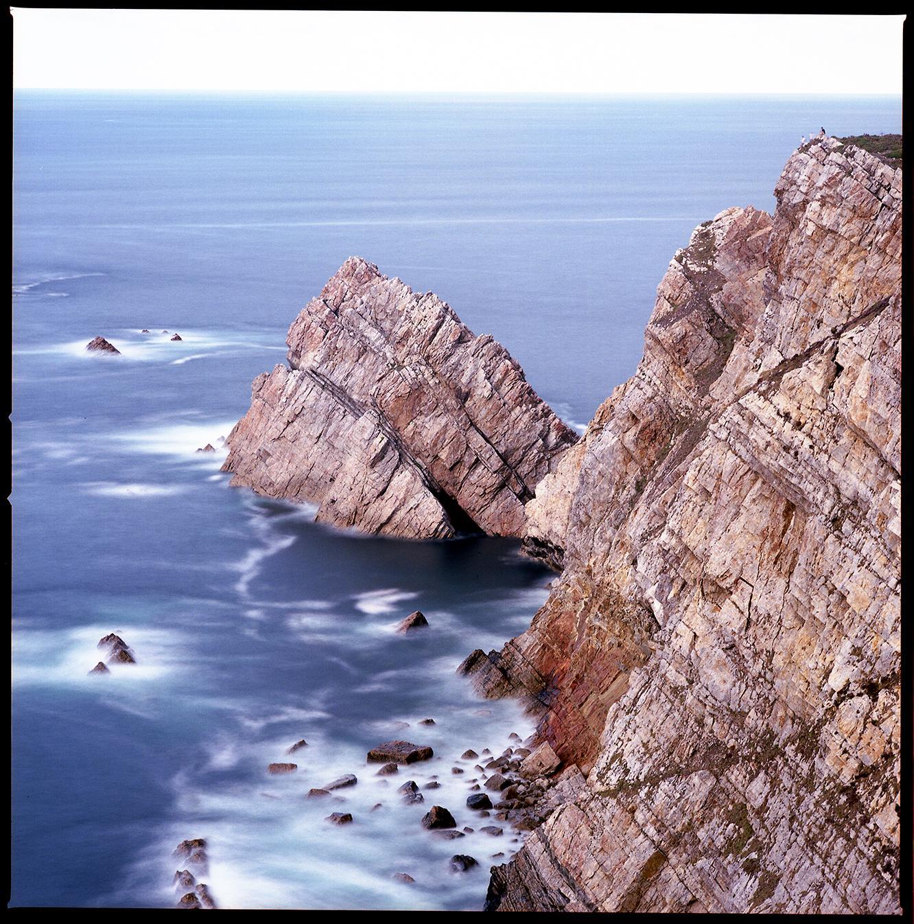 The ocean meets a rocky coastline with a long exposure blurring the water.