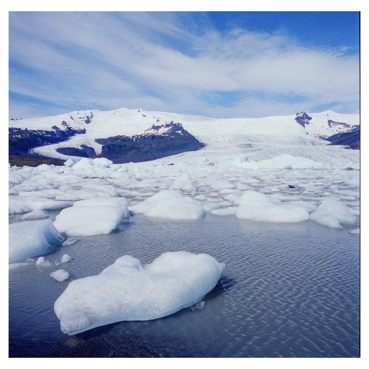 Icebergs float in a glacial lagoon with snow-capped mountains in the background under a blue sky.