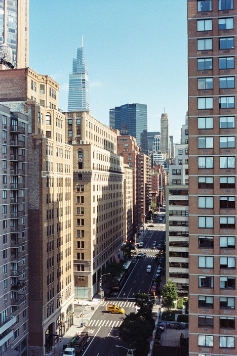 A high-angle view shows a street lined with tall buildings and a yellow taxi cab at an intersection.