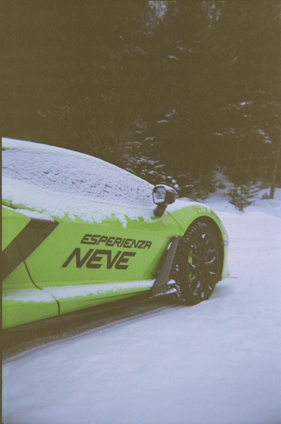 A bright green sports car with "ESPERIENZA NEVE" written on its side is parked in a snowy forest.