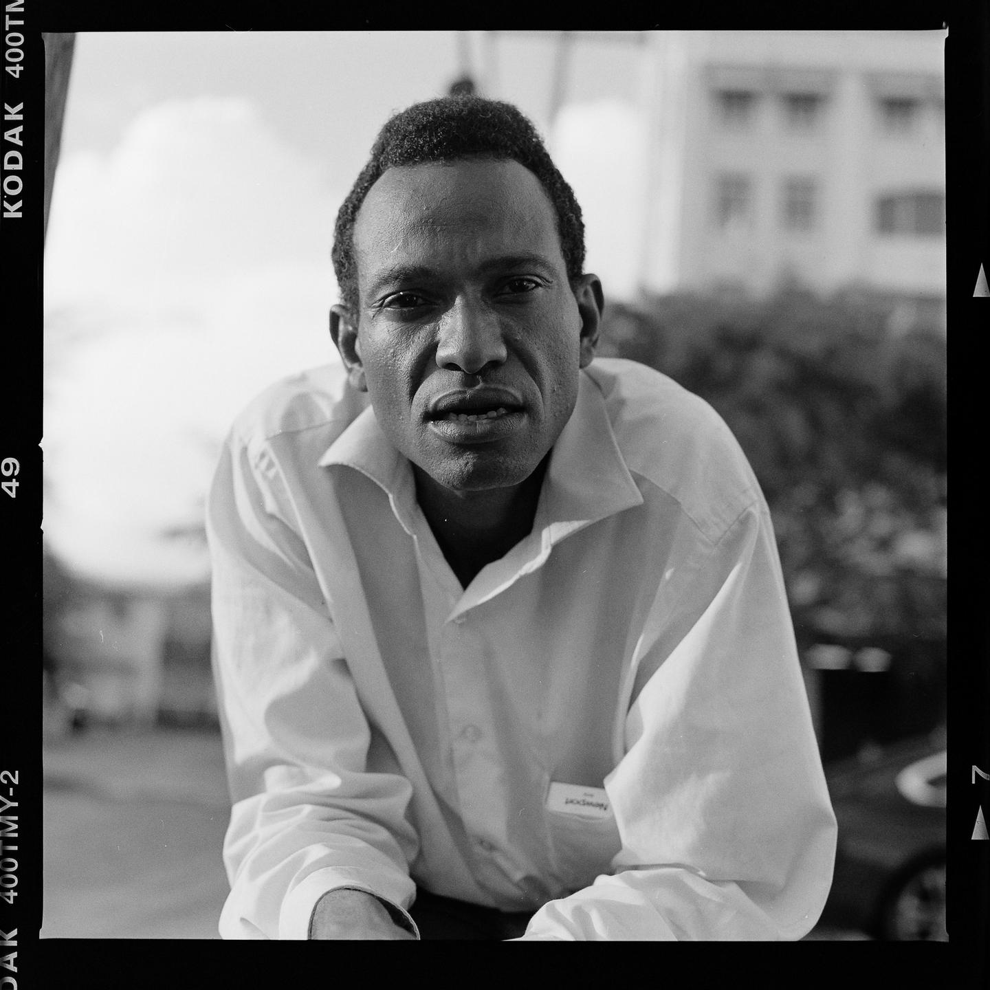A man in a white shirt looks directly at the viewer.