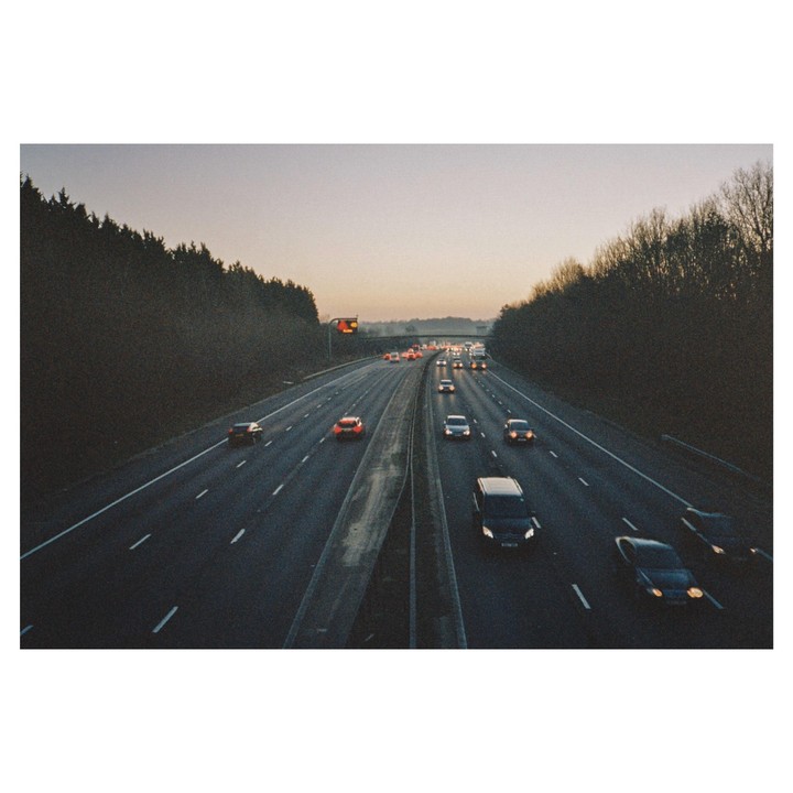 Cars drive on a highway lined with trees under a pale sky.