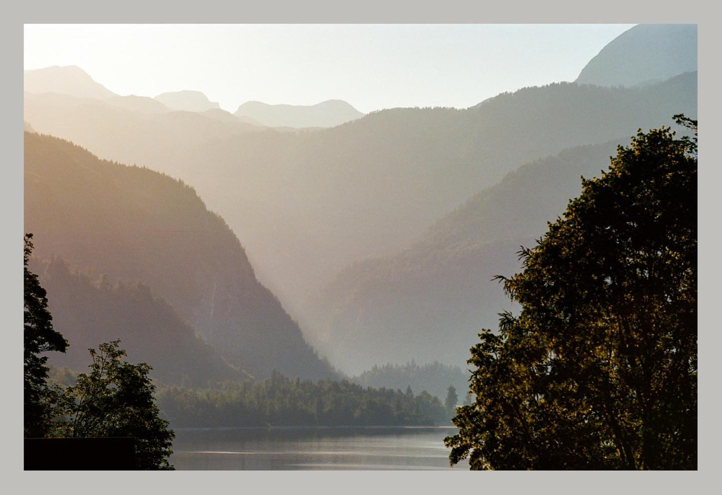 A body of water is surrounded by mountains and trees under a hazy sky.