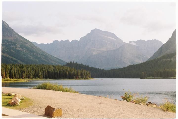 A lake is surrounded by a forest and mountains under a cloudy sky.