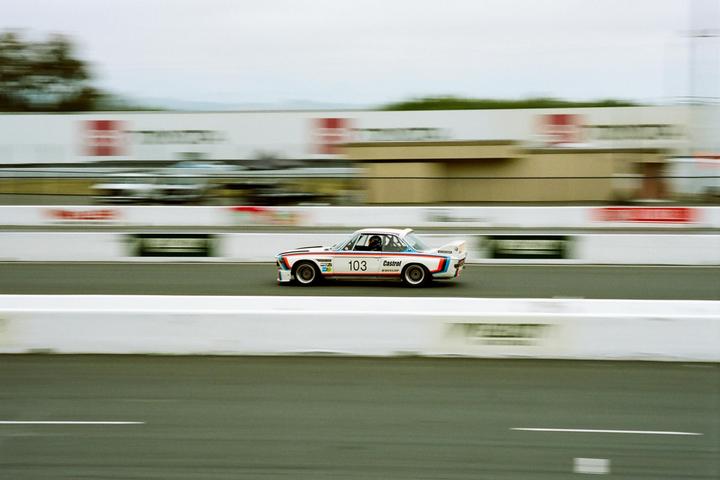 A white race car with red and blue stripes and the number 103 is speeding on a track.