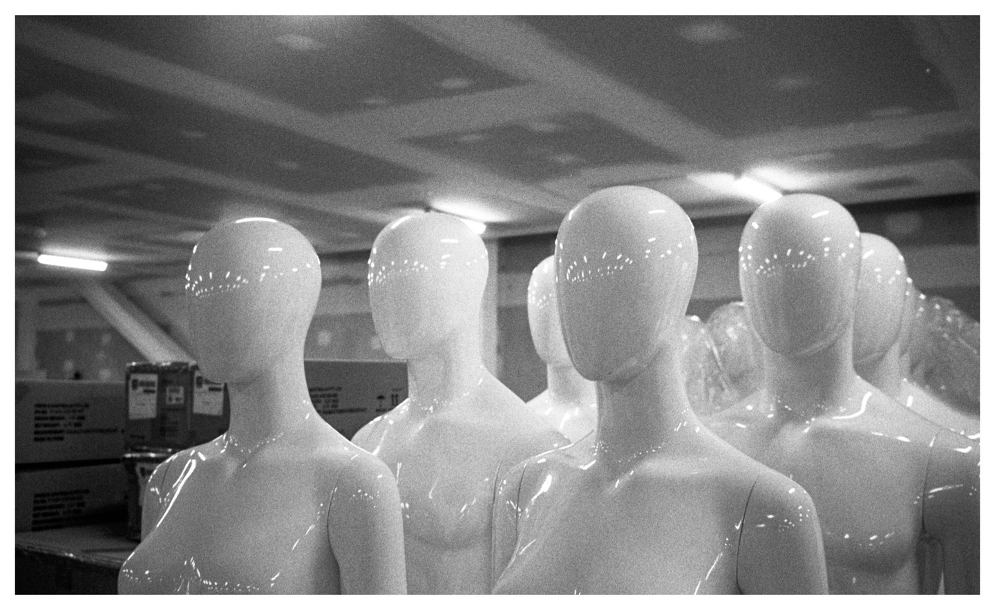 A group of shiny white mannequins are standing in a room with boxes in the background.