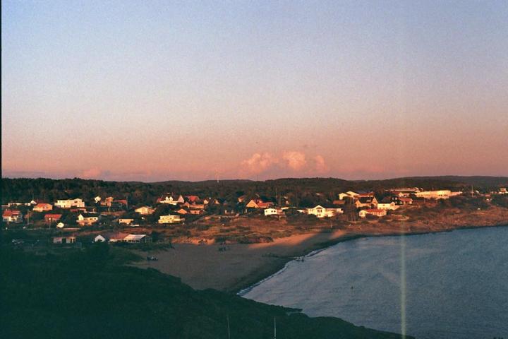 A coastal town with houses and a beach is visible under a colorful sky at dusk.