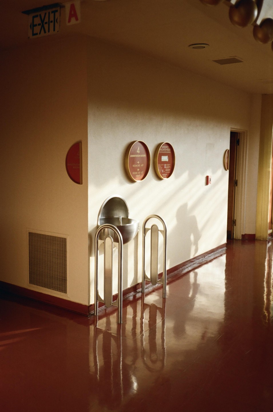 Sunlight casts shadows on a wall next to a water fountain and a shiny red floor.