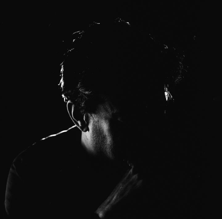 A man's head and shoulder are visible in a dark, high-contrast portrait.