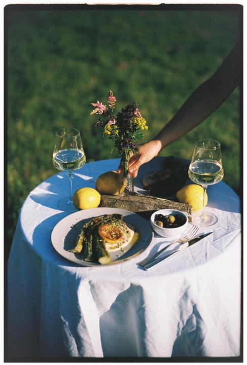 A hand reaches for a vase of flowers on a table set with food and wine glasses.
