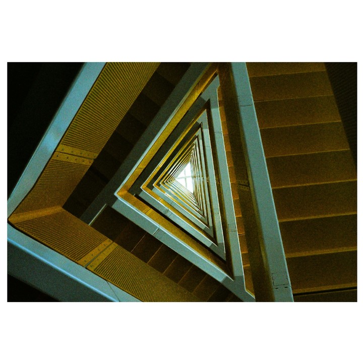 A low-angle view of a triangular stairwell shows repeating patterns of yellow steps and light blue railings.