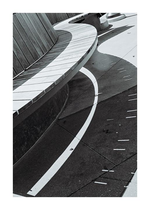 A curved wooden bench casts a shadow on the ground, which has a white line painted on it.