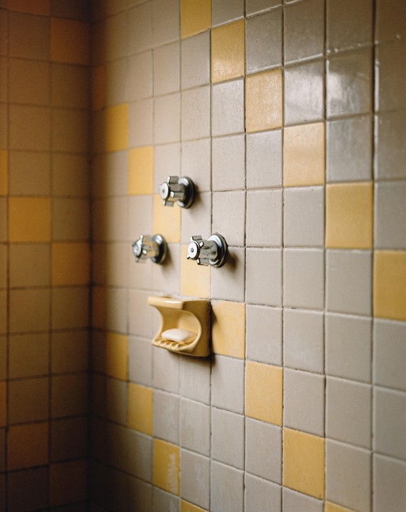 A yellow soap dish with a bar of soap is mounted on a tiled wall with three metal knobs.