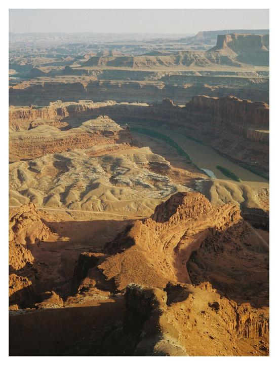 A vast canyon landscape with a river winding through it is visible under a hazy sky.