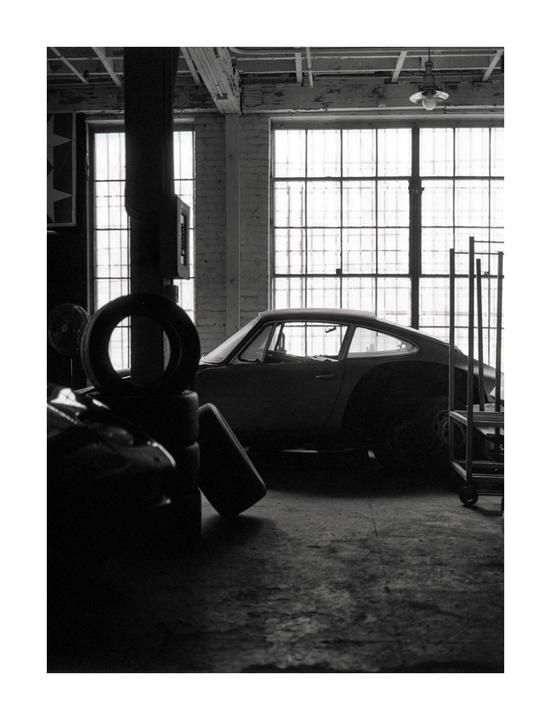 A classic car is parked in a warehouse with large windows.