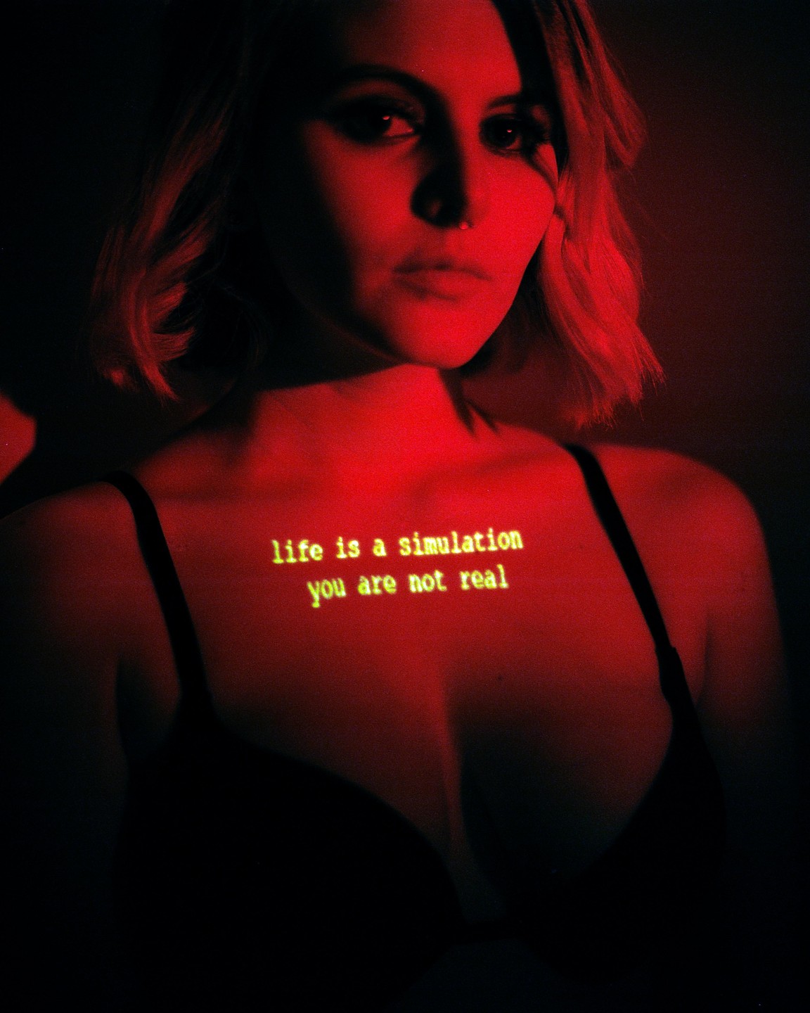 A woman is illuminated by red light with text projected onto her chest.