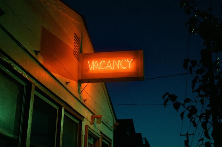 A neon "VACANCY" sign glows orange on the side of a building at night.