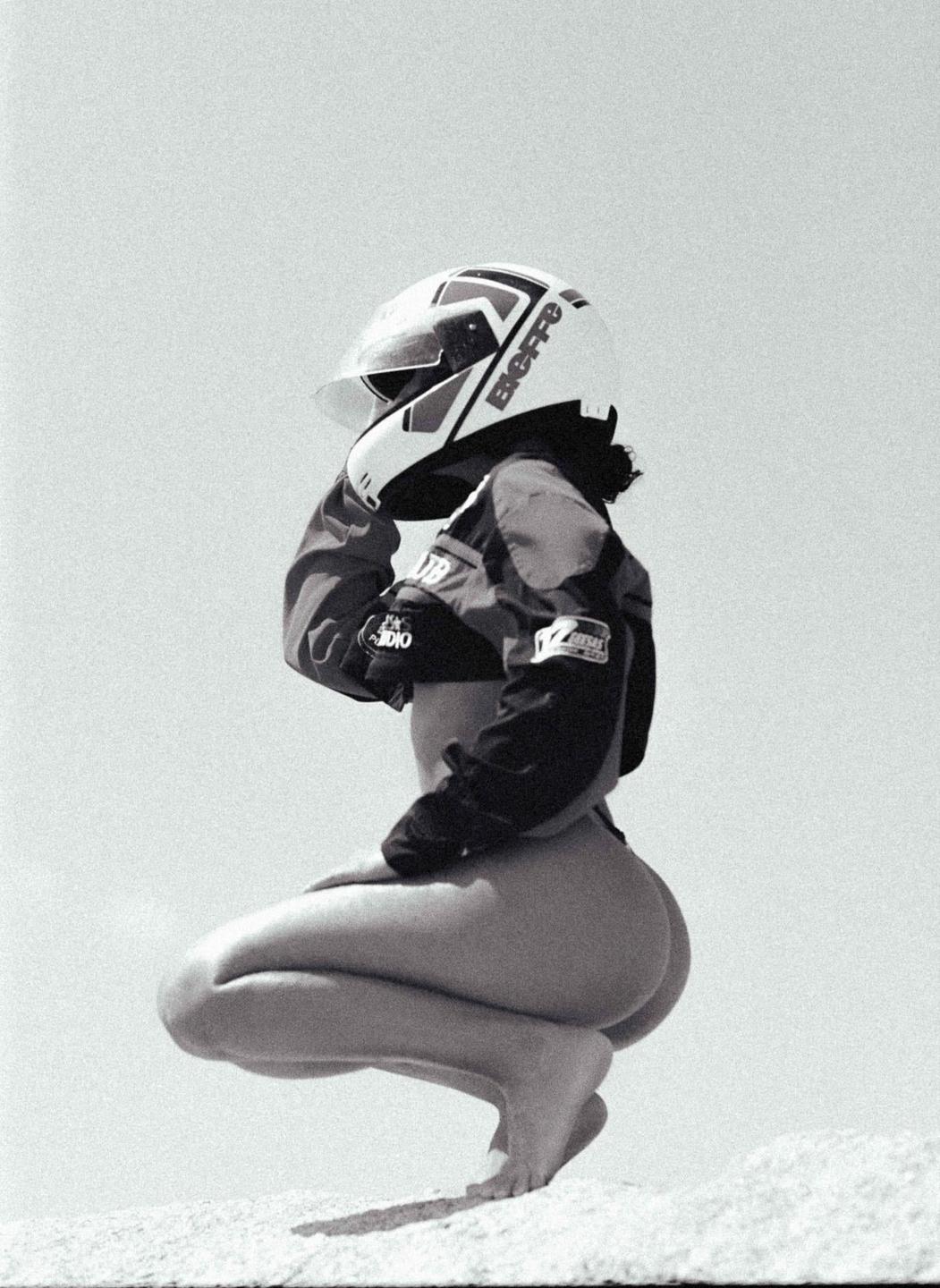 A woman wearing a helmet and jacket crouches on a light-colored surface.