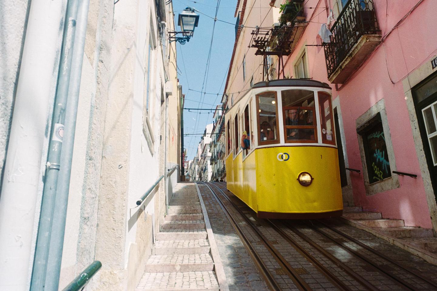 A yellow tram ascends a steep, narrow street lined with buildings in Lisbon.