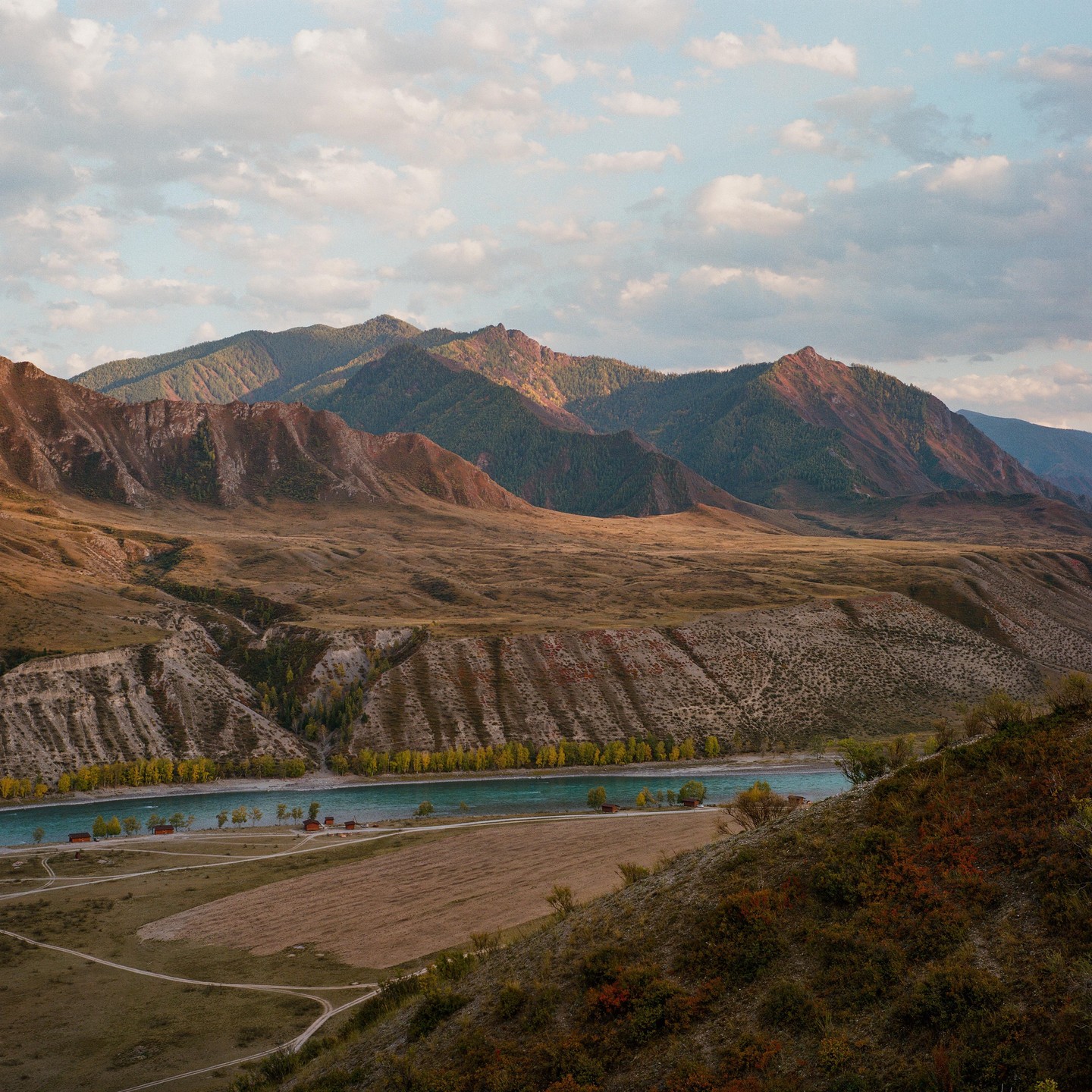 A river flows through a valley with mountains in the background under a cloudy sky.