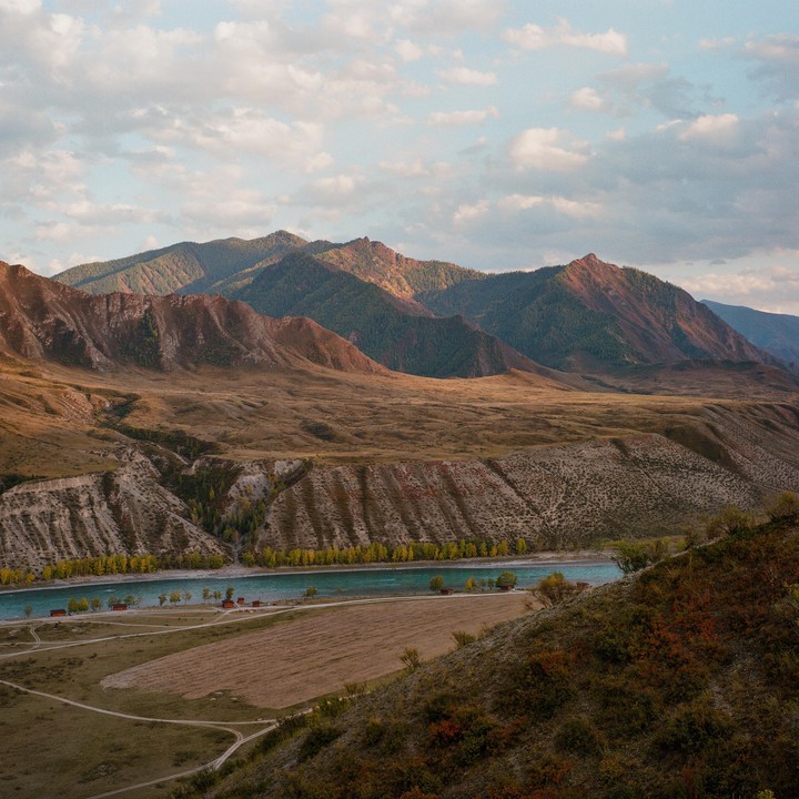 A river flows through a valley with mountains in the background under a cloudy sky.