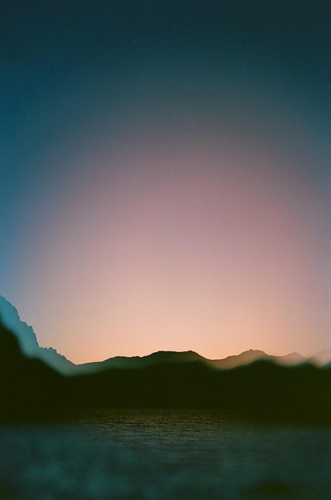 A body of water is in the foreground with silhouetted mountains and a colorful sky in the background.