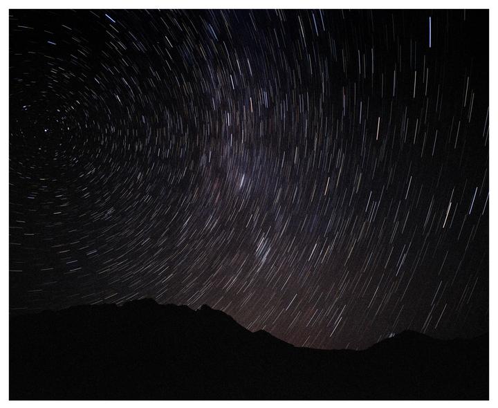 Star trails arc across the night sky above a dark mountain range.