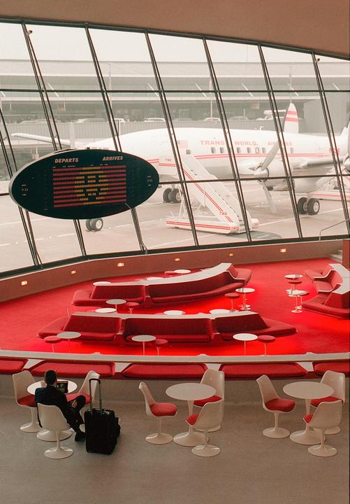 A man sits at a table in an airport lounge with a plane visible through the window.