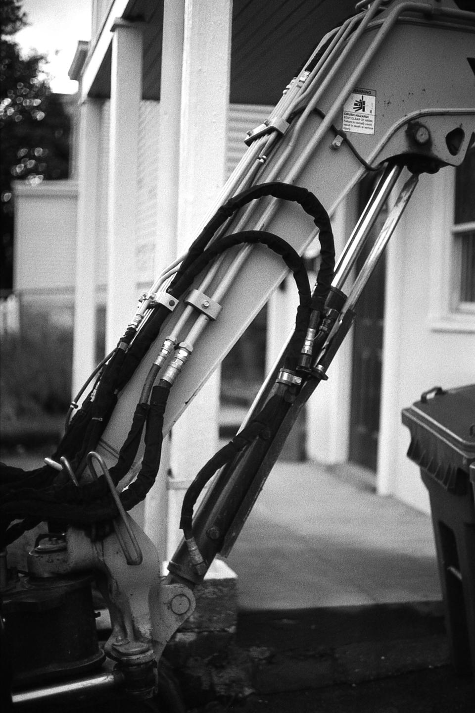 A close-up view shows the hydraulic arm of an excavator with hoses and cylinders.