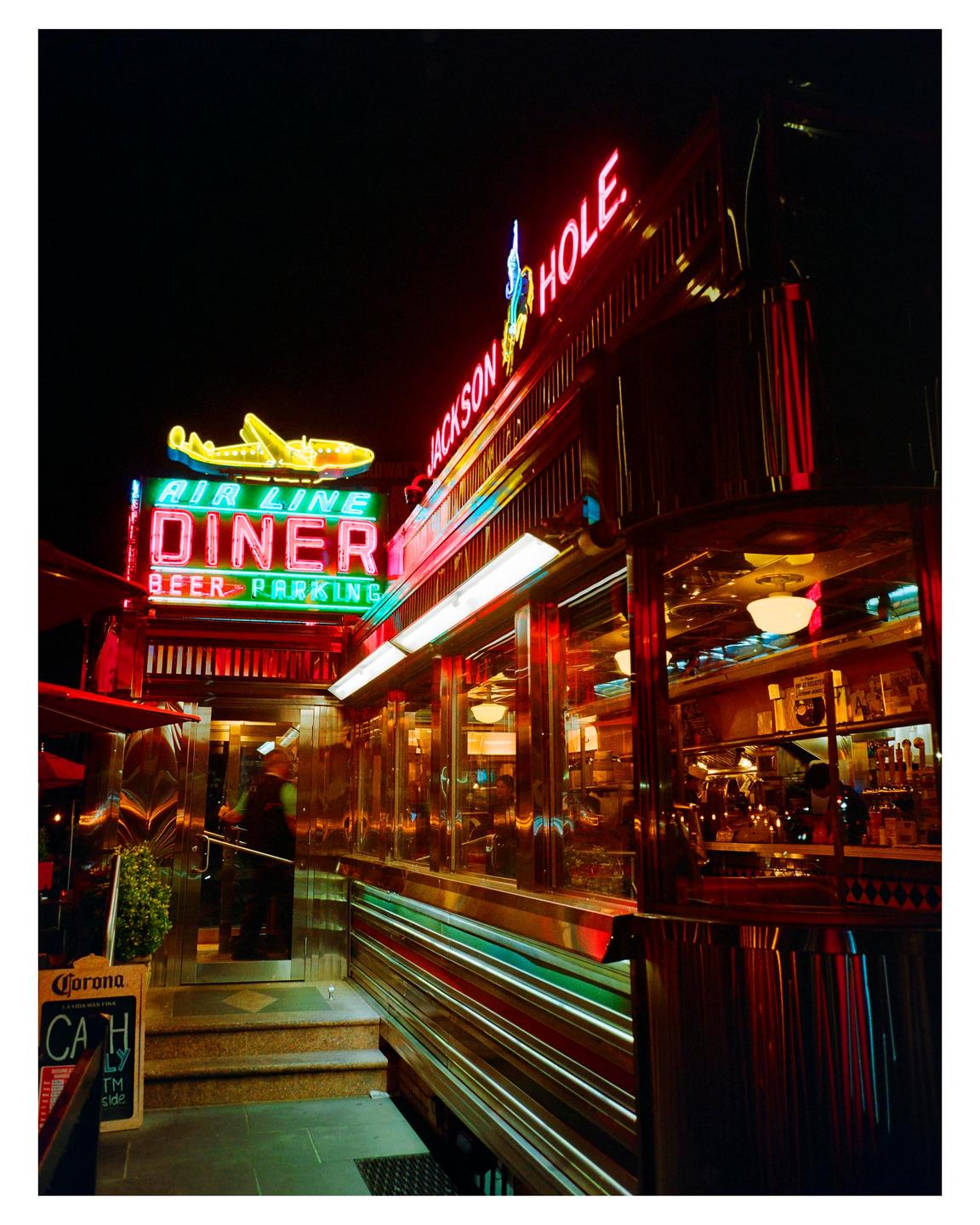 A diner with neon signs and a bright yellow airplane sign is illuminated at night.