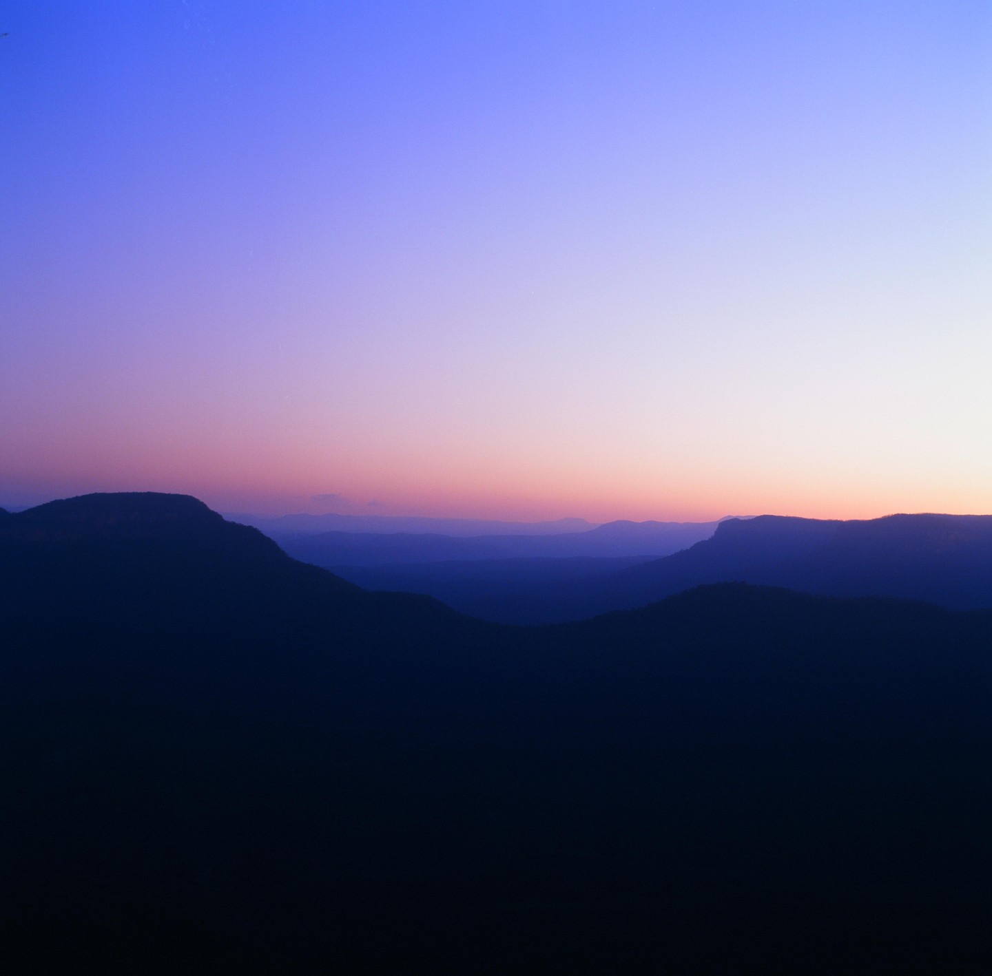 A mountain range is silhouetted against a colorful sky at dusk.